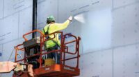 A construction professional spray painting the side of a building.