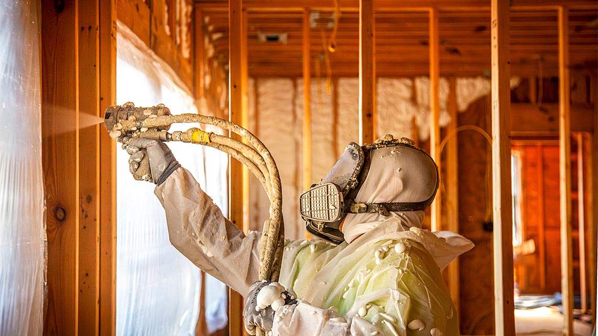 A worker in protective gear applying spray foam