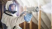 A man in a full hazmat suit using a sprayer