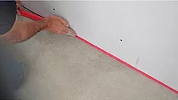 A contractor places joint tape between a wall and the floor