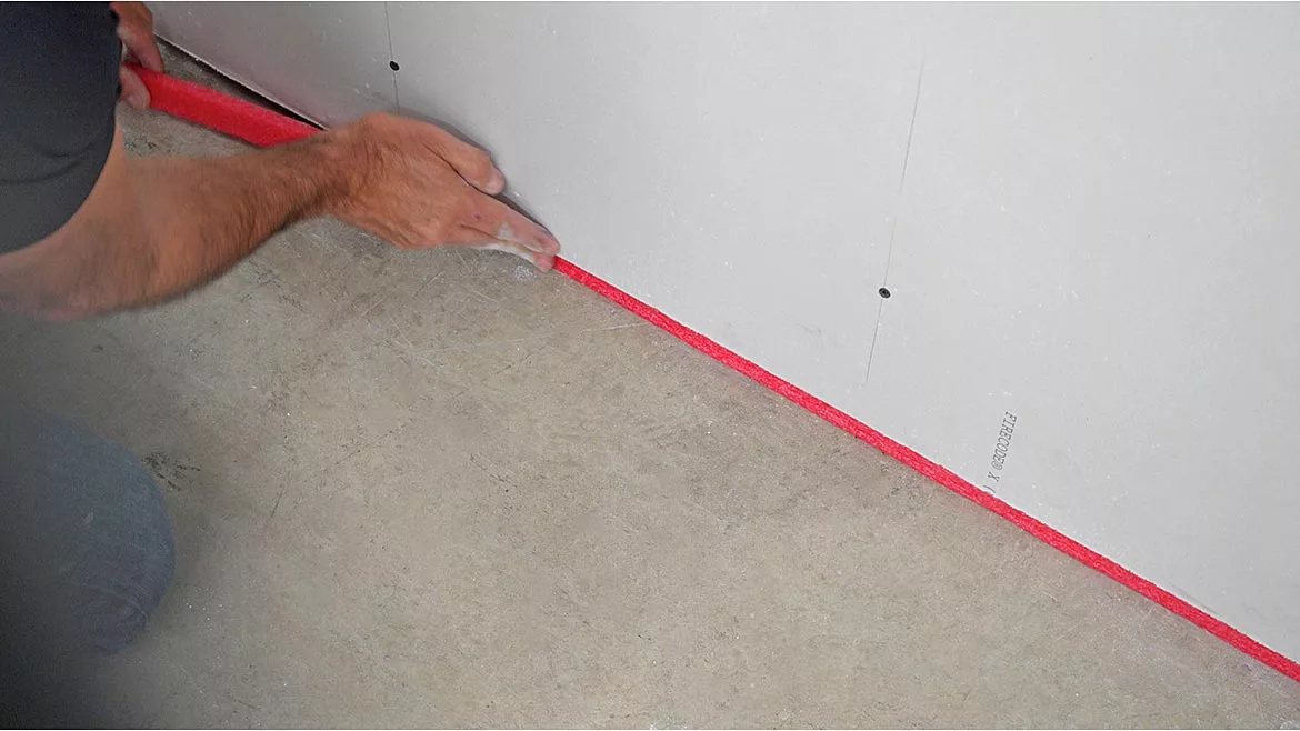 A contractor places joint tape between a wall and the floor