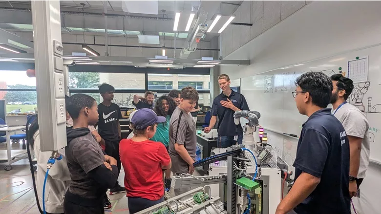 A group of kids and instructors gathered around a robot