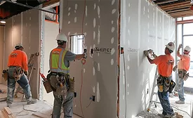 Construction workers in safety vests install drywall