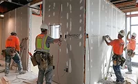 Construction workers in safety vests install drywall