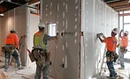 Construction workers in safety vests install drywall