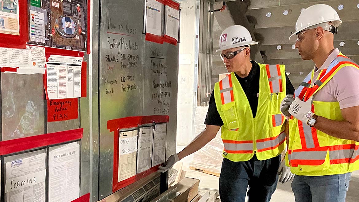 2 construction workers looking at a bulletin board on a job site