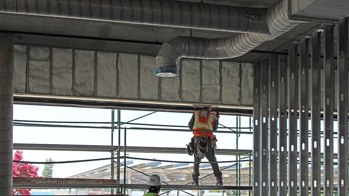 A construction worker on a scaffold. Steel framing and ventilation are also visible
