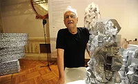 Frank Gehry standing beside a detailed architectural study model used to develop the digitally driven construction methods that influenced modern building delivery.