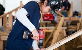 young woman wearing hardhat drills into a piece of wood