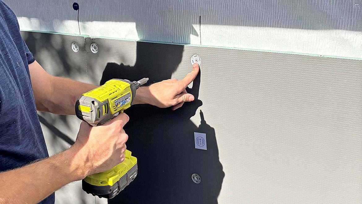 A hand holding a drill that is attaching HydroBlok panels